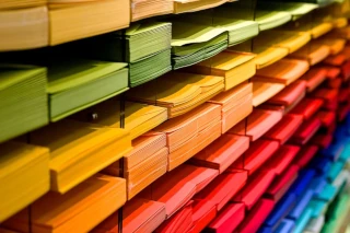 Stock image of coloured paper organised on multiple shelves of a rack.